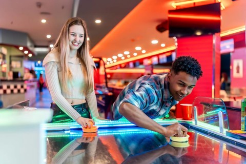 Happy diverse friends enjoying a weekend playing air hockey in a colorful entertainment center