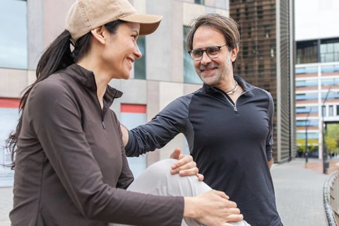 A vibrant couple dressed in athletic wear enjoys a friendly moment outdoors, preparing for a sports