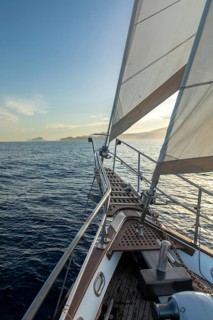 A tranquil scene of a sailboat navigating the calm waters of the Mediterranean Sea at sunrise, with