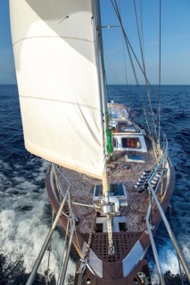 A sleek yacht sails through the Mediterranean waters, its sail full and the sun casting a golden