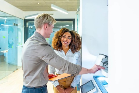 Two colleagues using a multifunction printer in a modern coworking office, collaborating and
