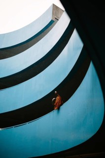 An unrecognizable woman with vibrant red hair stands at a balcony of a blue parking lot. The unique
