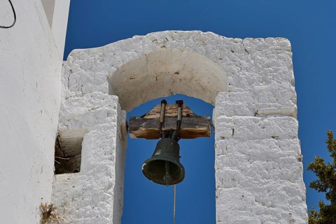 Taxiarchis, Church of the Archangel, close-up of a bell under a stone arch against a blue sky,
