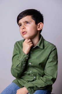 A young boy wearing a green shirt and blue jeans is sitting thoughtfully, with his hand on his