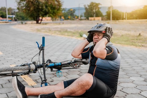 Cyclist on the pavement with a headache. Concept of cyclist suffering with migraine. Male cyclist