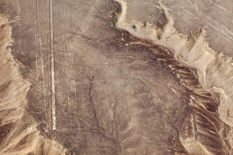 Aerial view of a sandy area with visible patterns and lines, surrounded by sloping terrain, the