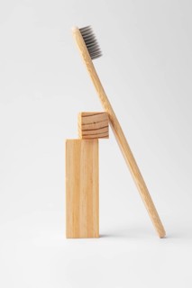 A natural bamboo toothbrush elegantly leans against two stacked wooden blocks. The minimalist