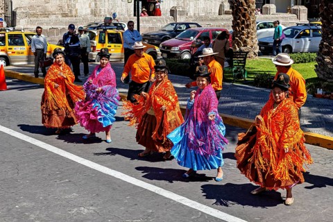 Women in traditional colorful clothes dance energetically on a busy street, a colorful dance and