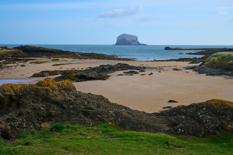 Extensive coastal landscape with rocks, sand and sea views under clear skies, Bass Rock, North