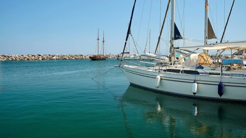 Sailing boats calmly moored in the harbour with clear blue water under a blue sky, Pali village,