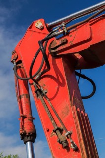 Electrical power and hydraulic fluid supply lines on hinged boom of red painted backhoe excavator,