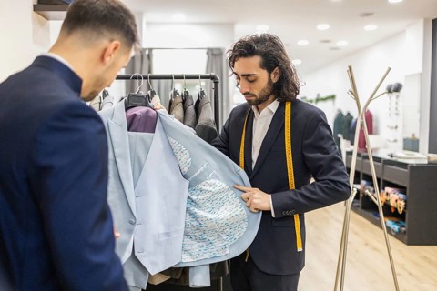 A skilled tailor presents a custom suit to a client in a suit store, highlighting detailed