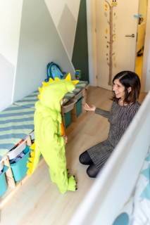 Mother playing with her son wearing a dinosaur costume in his bedroom, having fun together