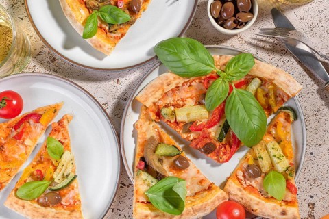 Rustic vegetarian pizza topped with fresh basil, zucchini, eggplant, peppers, and olives. Perfectly