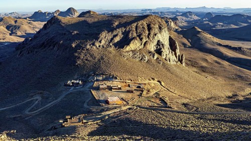 Small settlement at the foot of a large rock in a dry, barren region, The landscape of the Ahaggar