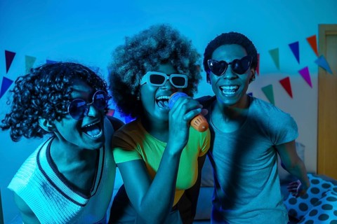 Multiracial friends singing karaoke partying at home at night with blue neon lighting