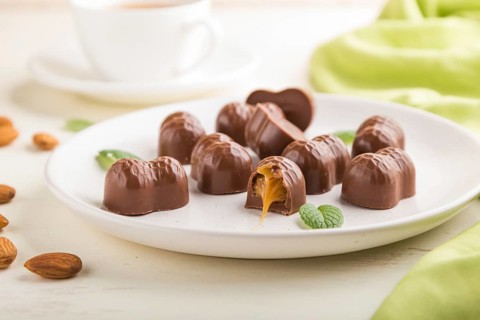 Chocolate candies with almonds and caramel on a white wooden background and green textile. side