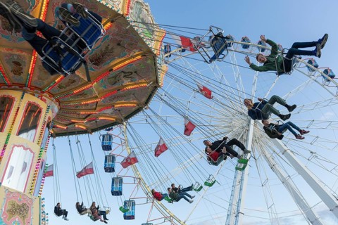 People swinging on a carousel in front of a Ferris wheel in sunny weather at a funfair, Europa Rad,