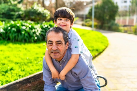 Grandfather giving his grandson a piggyback ride in a sunny park, enjoying quality time together