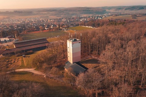 Wasserturm stands in a wooded area near a village, the picture is in yellow-orange tones,