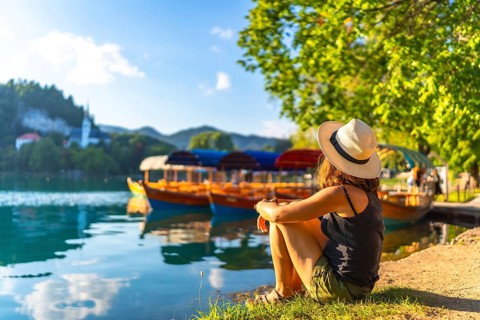 Young woman in summer attire and hat relaxing by lake bled in slovenia, enjoying views of