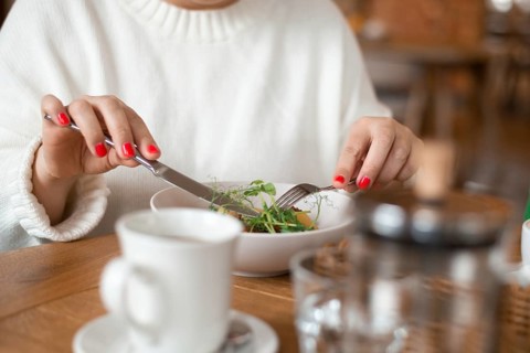 Close-up of a woman savoring a breakfast dish with a cozy ambiance in a cafe. The table setting