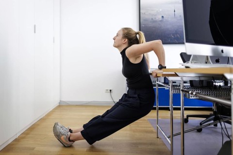 A woman does sports exercises at her workplace in an office in Berlin, 08/08/2024