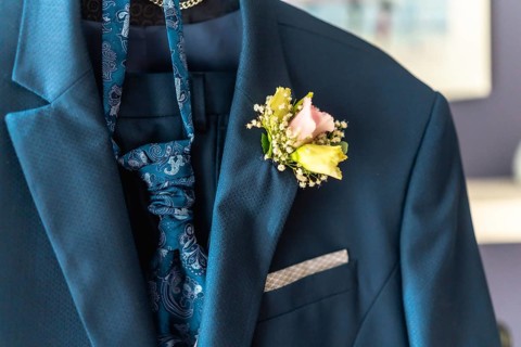 A man's blue suit jacket is adorned with a boutonniere of pink and yellow flowers