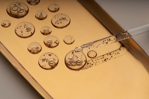 Close-up view of a dropper dispensing anti-aging facial serum with suspended golden particles onto