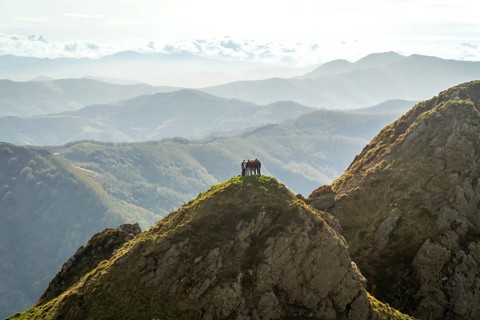 Hikers stand on the summit of aiako harria, part of the penas de aia mountain range, enjoying the