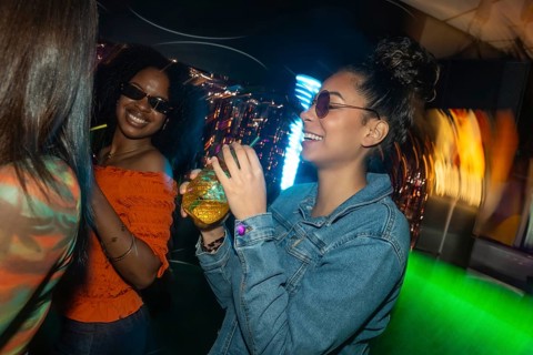 Group of diverse friends celebrating and dancing in a vibrant club, smiling and drinking cocktails