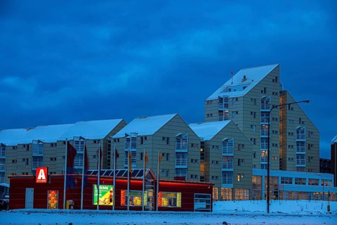 Illuminated supermarket at dawn, behind it apartment buildings in modern architecture, Reykjavik,