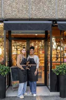 Two workers in aprons stand in front of a cosmetics store, smiling confidently, showcasing a