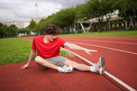 Young caucasian man stretching legs before running in an outdoor running track