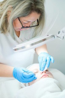 Esthetician cosmetologist uses a metal extractor tool for deep pore cleansing, removing blackheads