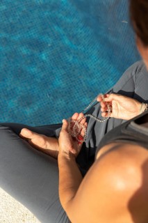 From above cropped unrecognizable woman practicing yoga beside a swimming pool, holding a string of