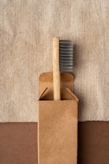 Top view of a bamboo toothbrush partially in a brown cardboard box, set against a textured beige