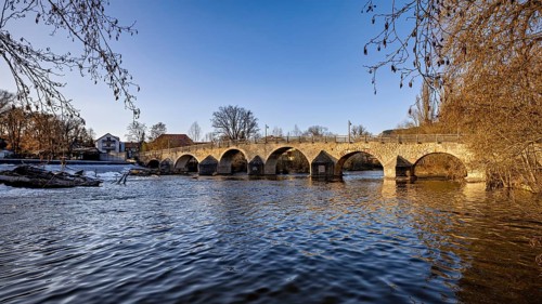 Stone bridge over a river in daylight surrounded by winter nature, The Burgau Bridge in the Saale