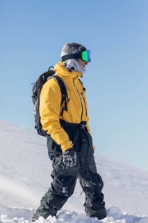 Snowboarder dressed in a yellow jacket and dark pants, equipped with goggles and backpack,
