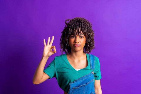 Studio portrait capturing a young woman making an okay gesture with her hand against a vibrant