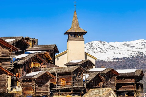Snow-covered roofs of old farmhouses and barn storage, in the back the church tower of the Saint