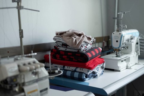 A sewing workshop showcasing colorful fabric stacks on a worktable, with a sewing machine in the