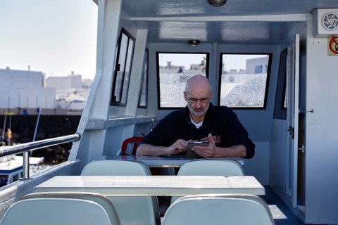 Tourist sitting on an excursion boat and reading a tablet, Orzola, Lanzarote, Spain