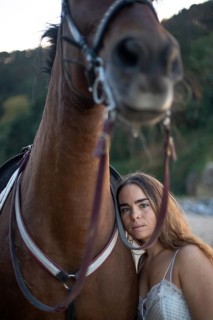 A young woman stands calmly with her horse in a tranquil environment, embodying harmony and mutual