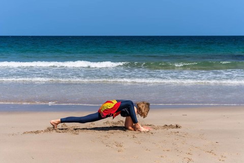 A woman doing yoga on a sandy beach by the sea. Ashva Sancalanasana, hip opening, variation. Treen