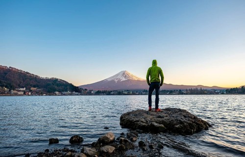 Young man standing on rocks in Lake Kawaguchi, view of Mount Fuji volcano at sunset, Yamanashi