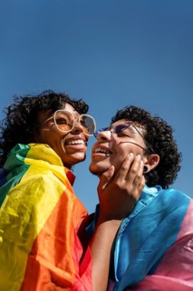 A joyful LGBTQ+ couple sharing a loving moment under a clear sky, wrapped in a rainbow flag,