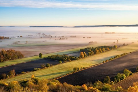 Scenics view of a beautiful rural landscape with fields and low morning fog at sunrise in autumn