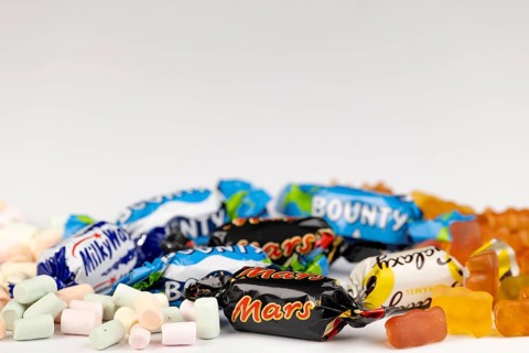 Various sweets including marshmallows, gummy bears and chocolate bars on a white background