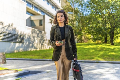 Young arab entrepreneur walking along street with trees carrying laptop bag and mobile
